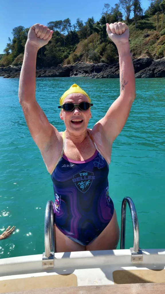 Jo Norman raising both arms in celebration on the boat ladder after the Jersey to France to Jersey swim